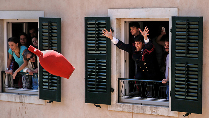 Man throwing large red pot from window in Corfu Greece Celebrating Easter