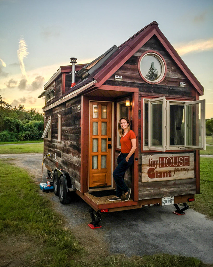 Small house on wheels with girl in front of it