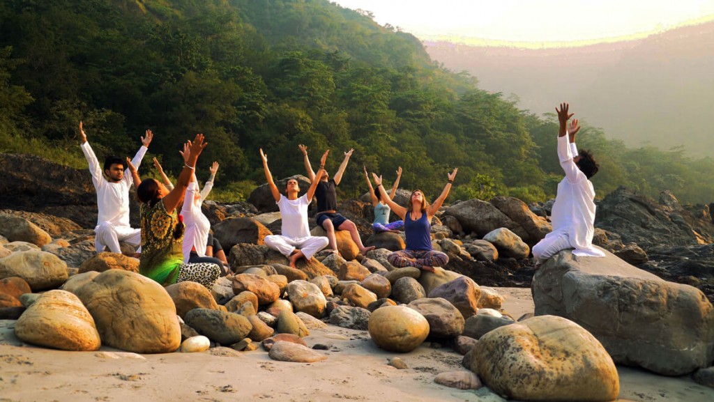 People practicing yoga sitting on rocks at the beach