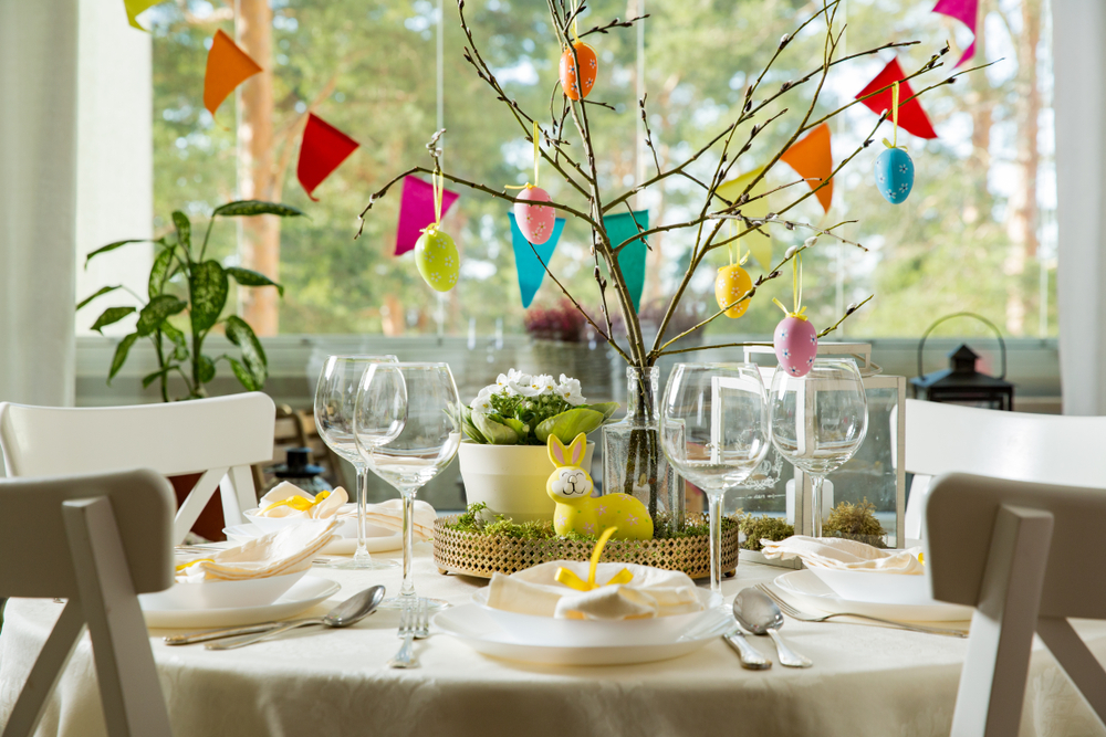 Tree branches with Easter eggs hanging and a plastic bunny in front of it put on a table