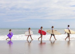 Rear view of family mother, father, daughter, parents and female girl children going surfing with surfborards on a sunny vacation day