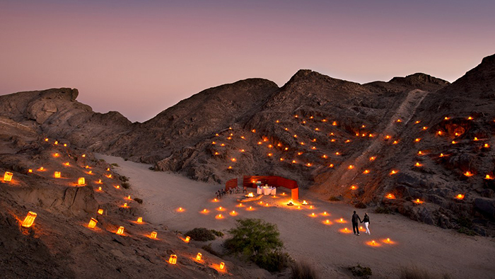 Romantic candles around the small hills and a couple reaching their dinner table