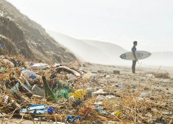 Polluted beach with plastic and a surfer