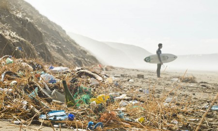 Polluted beach with plastic and a surfer