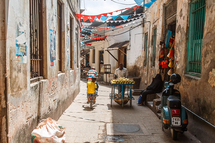 Small street in Stone Town with kids on a bike and a street vendor