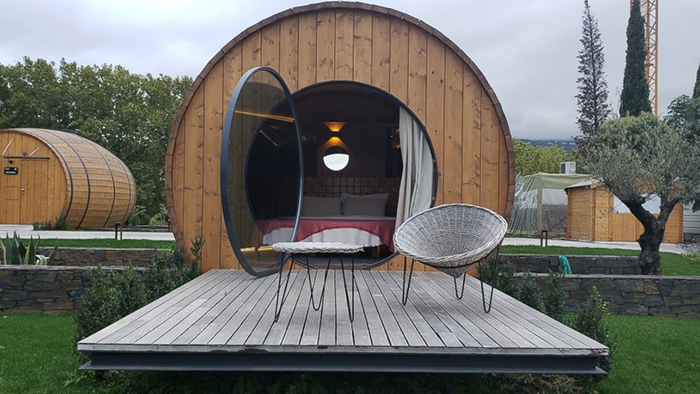 Wine barrel with wide open glass door and a small balcony in front of it with wooden table and chair 