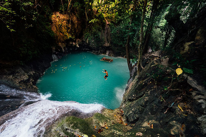 Man jumping in a waterfall surrounded with trees and rocks