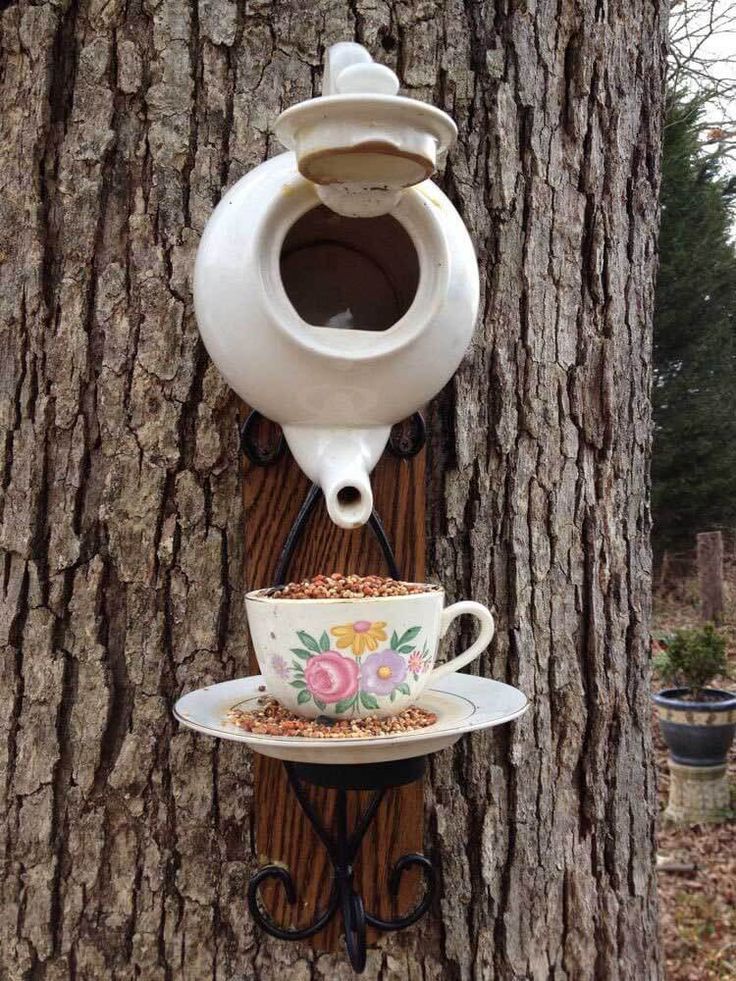 Bird feeder made of tea kettle and a tea cup hanging on a tree