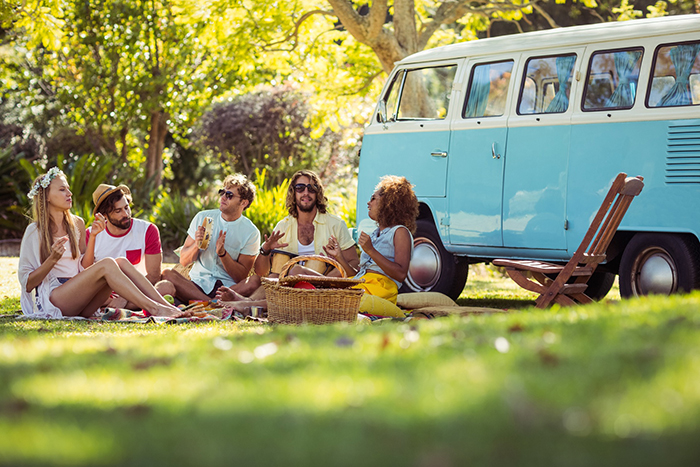 Group of friends having picnic in a meadow and their retro bus behind them