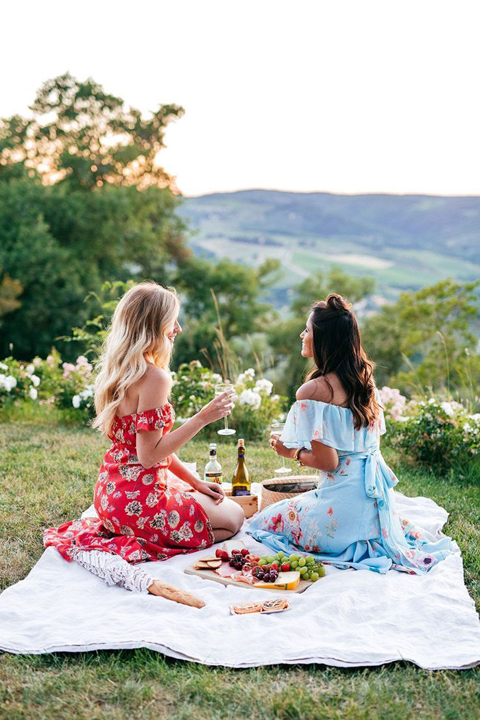 Two girls in dresses enjoying a glass of wine while doing picnic