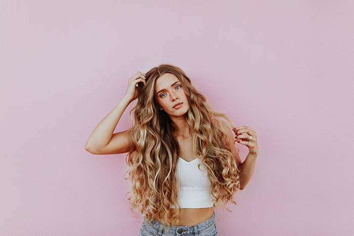 Blonde woman with long curly hair standing in front of pink wall