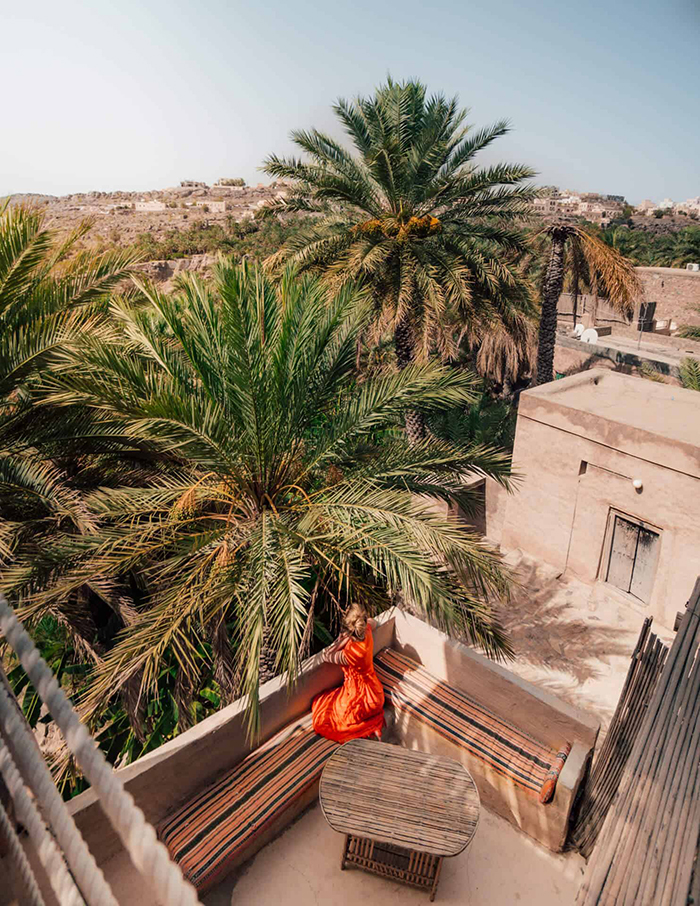 Woman sitting on the balcony of an old house with a view on palms