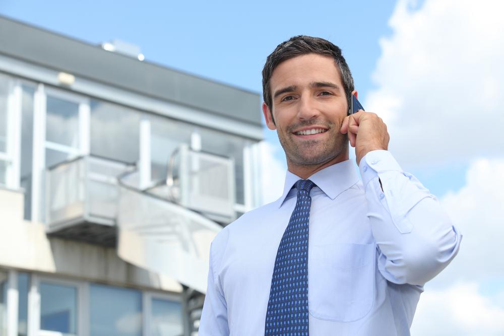 Man landlord with tie smiling and talking on the phone in front of his new property