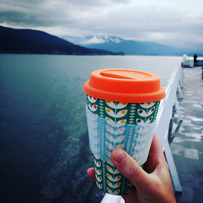 Person holding reusable travel mug with a nice ocean view behind