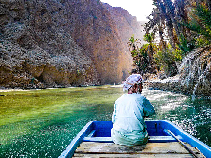 Old man on a boat surrounded with palms and rocks