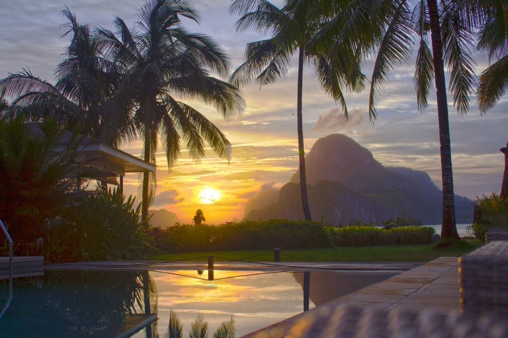 Beach house with a pool palm trees around and the sunset in the distance