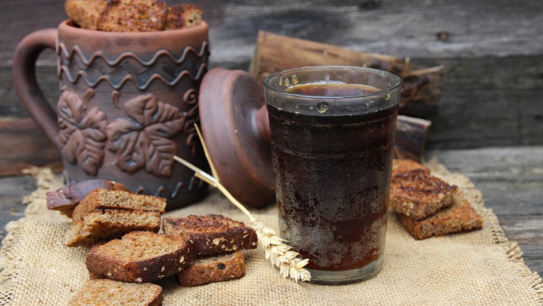 A glass full of kvass and rye bread around it