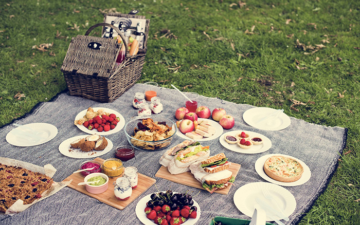 Picnic blanket full of different kinds of food like snacks and fruits