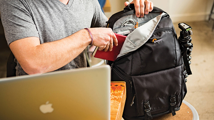 A person putting a notebook in a multiple compartments backpack