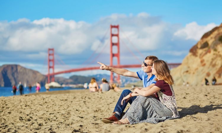 Couple enjoying the sun at the beach and the Golden gate Bridge in the bakcground