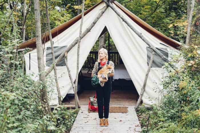 Woman holding a dog and standing in front of their glamping tent