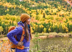 Autumn hiker girl outdoor in nature forest lake backpacking for camping travel trip. Happy Asian woman hiking outdoors with bag and hat, cold outerwear gear.