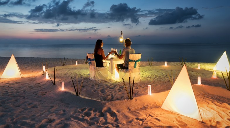 Couple enjoying a romantic dinner on a beach with candles around