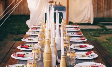 Summer party table decorated with candles in bottles and decorated jars instead of glasses