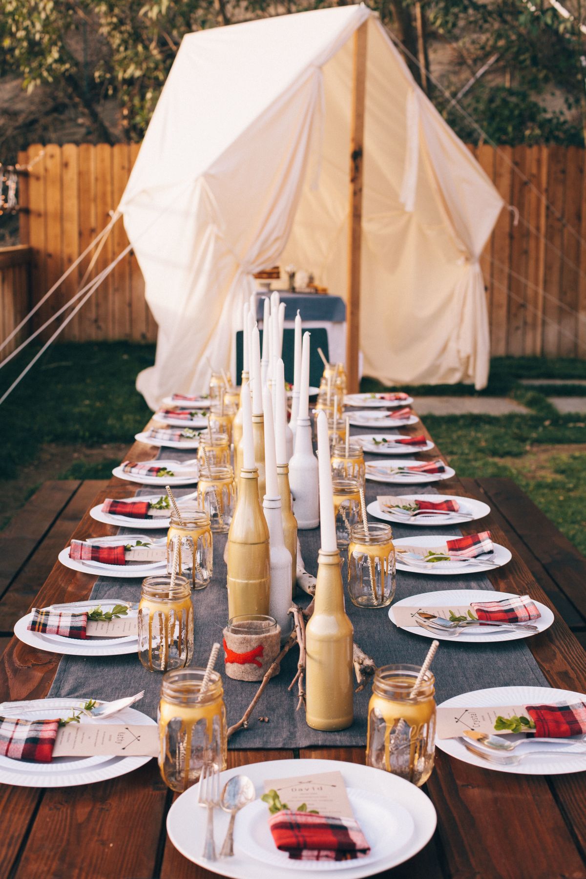 Summer party table decorated with candles in bottles and decorated jars instead of glasses