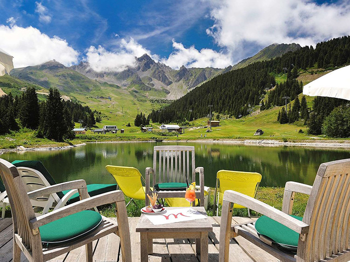 Wooden chairs and a table put in front of a small lake among the mountains in France