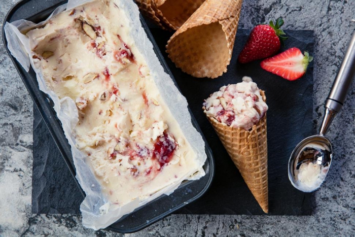 A container with homemade strawberry ice cream a spoon and cones