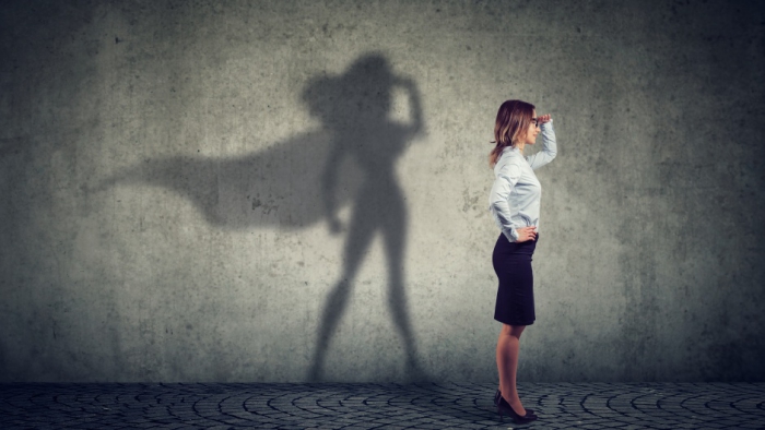 Woman with superwoman shadow on a wall