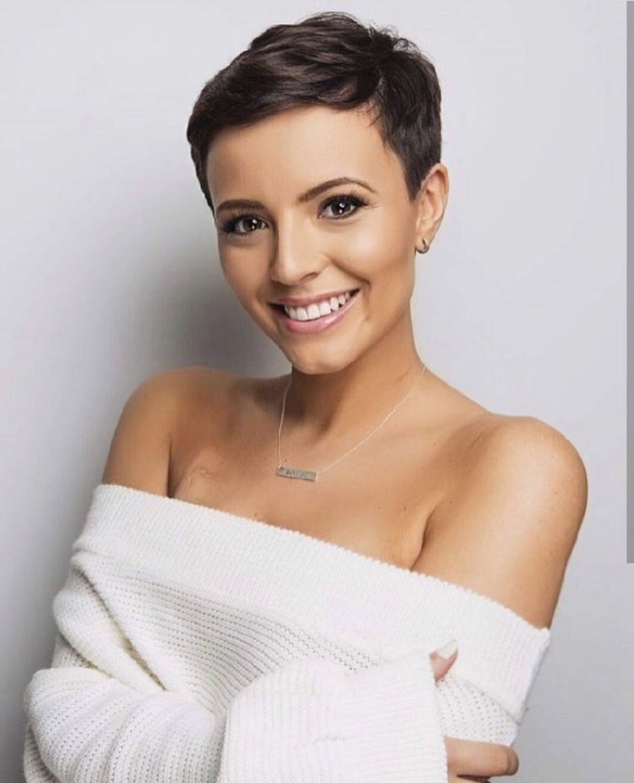 woman with short dark hair white sweater smiling on light background