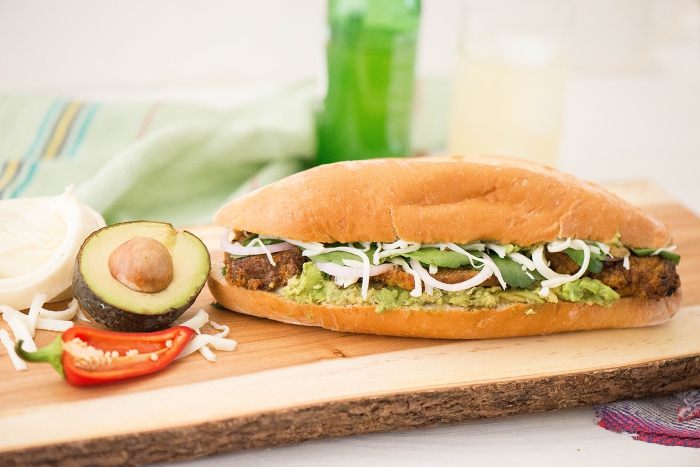 Mexican loncha sandwich on a wooden board with half avocado and chili pepper