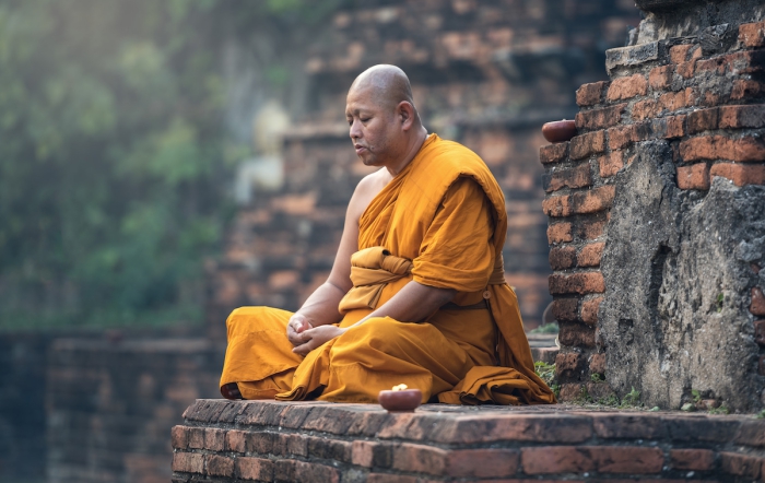 Buddhist monk dressed in orange meditating at the walls of a temple