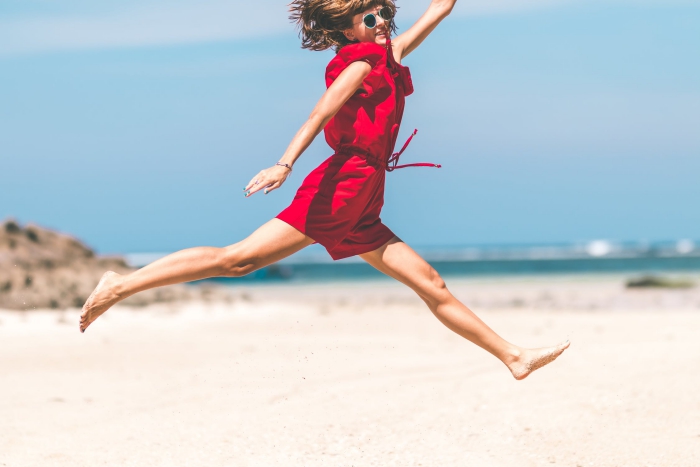 Woman in red dress jumping on beach