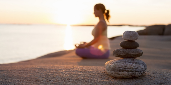 Woman meditating at sunrise on a lake shore- stones close up