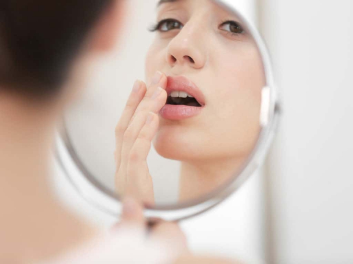 Woman looking herself in the mirror touching her lips oral fungal infection