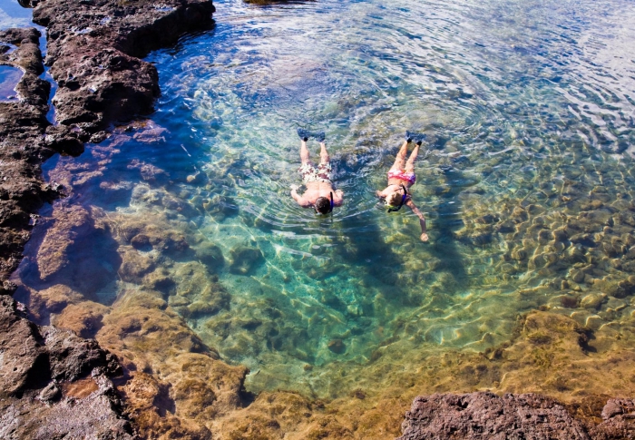 Couple snorkeling in rocky shore in crystal clear water