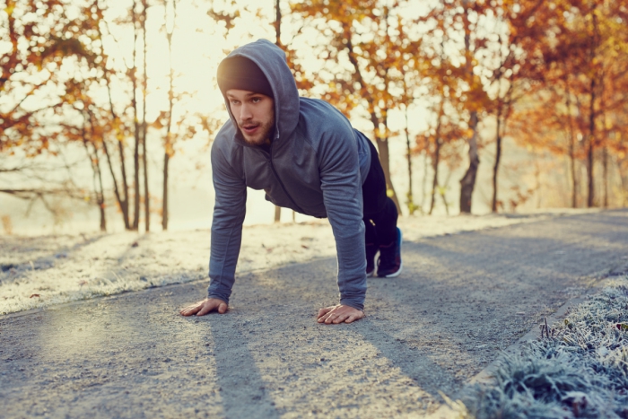 Young runner dressed in grey doing push ups exercise during cold autumn morning