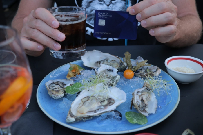 Person showing Chase Sapphire Preferred card on a table oyster plate drink lunch