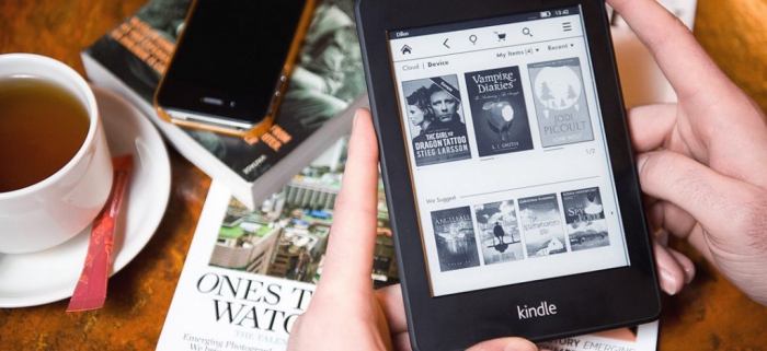 hands holding an e-reader desk background with books and cup of tea