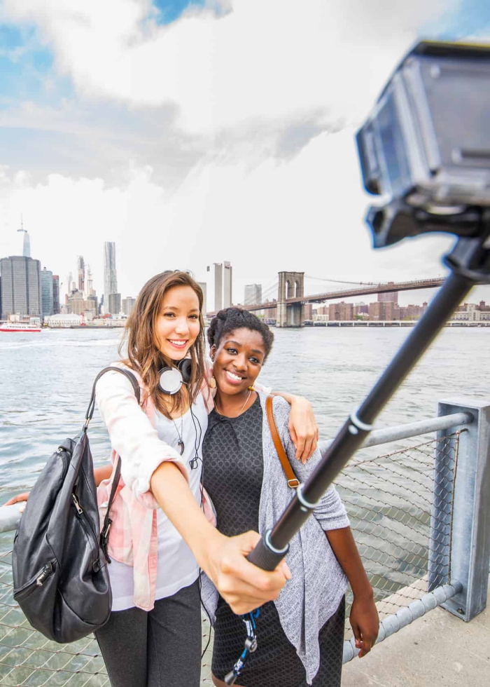 two girls taking a picture with a selfie stick on a river