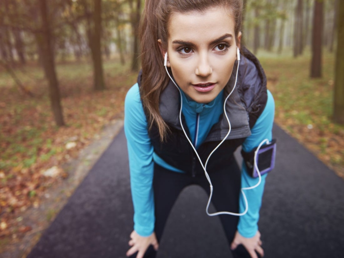 Woman with brown eyes jogging in a park with headphones and phone