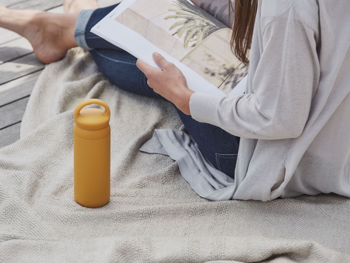 travel gift ideas woman reading a magazine with a yellow thermos bottle