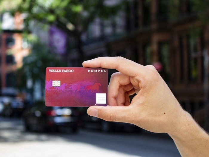 Hand holding Wells Fargo Propel American Express card city street background