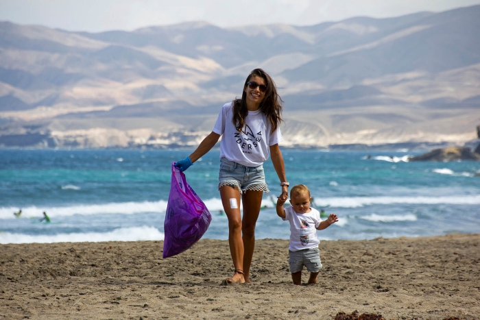 woman and baby walking on the beach cleaning with purple trash bag