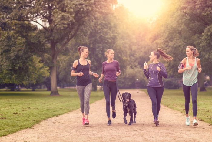 Four Healthy Young Women Jogging at the Park in the Afternoon with a dog