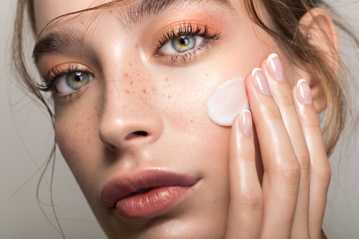 Woman with light green eyes close up applying ceramide cream