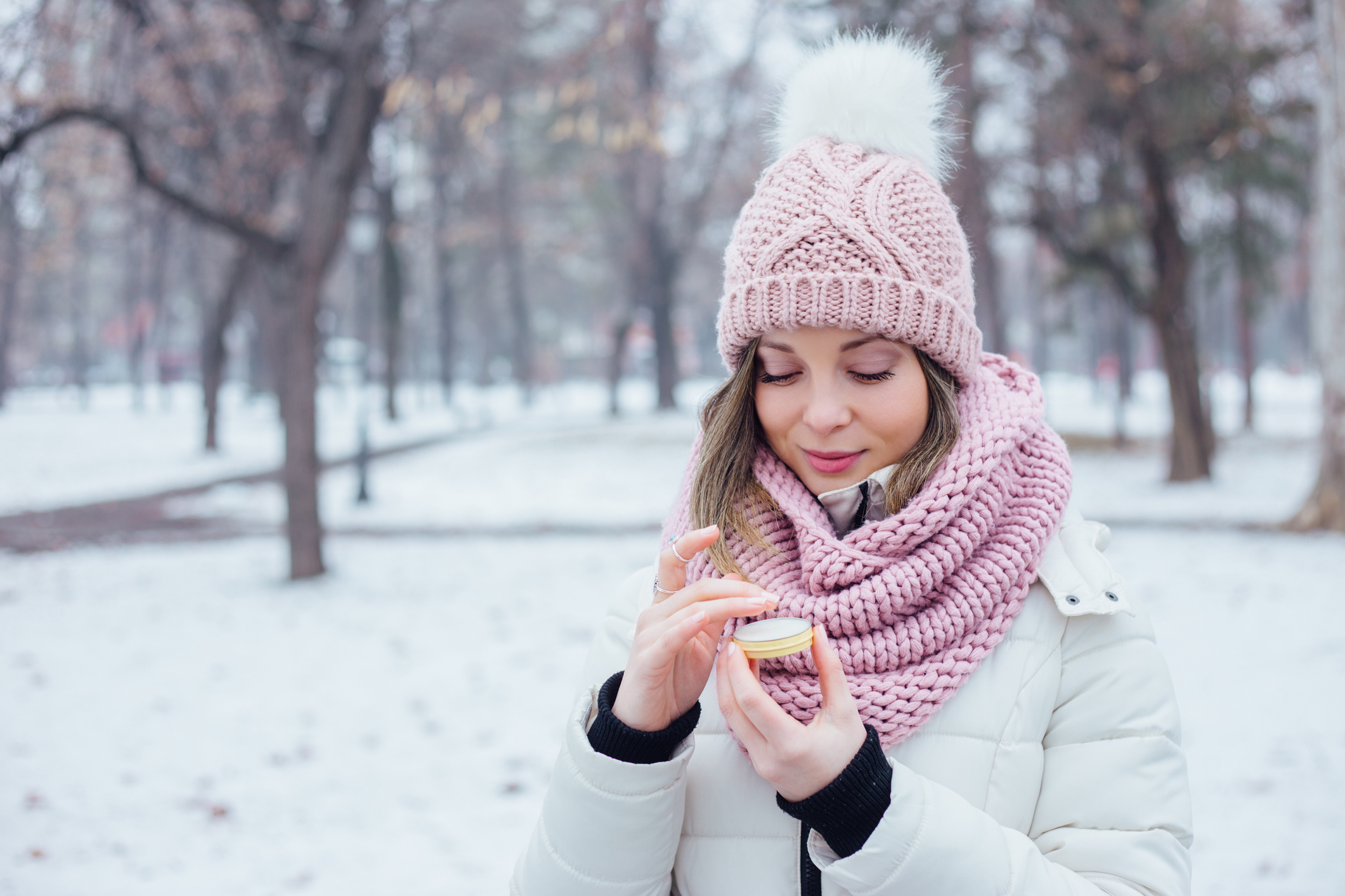 Young woman in winter clothes apply lip care balm outside cold snowy weather